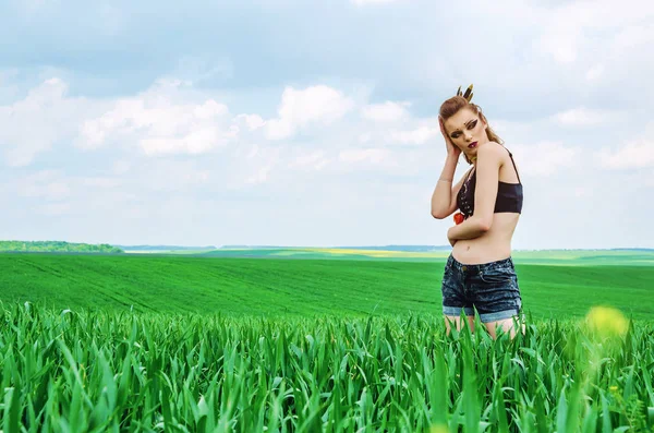 Girl with Amazon make-up stands in field among green wheat — Stock Photo, Image