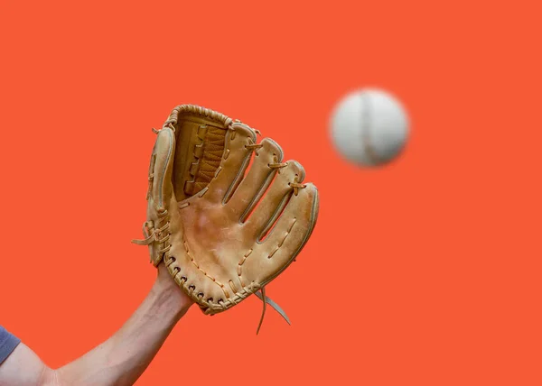 Mão em uma luva de beisebol de couro pega uma bola branca no desfoque em um fundo vermelho — Fotografia de Stock