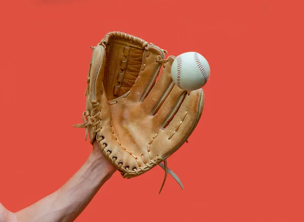 Hand in a leather baseball glove catches a white ball in defocus on a red background — Stock Photo, Image