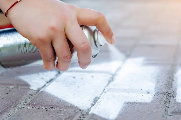 Mannelijke hand houdt een spuitbus spray kan, tekent graffiti op het asfalt — Stockfoto