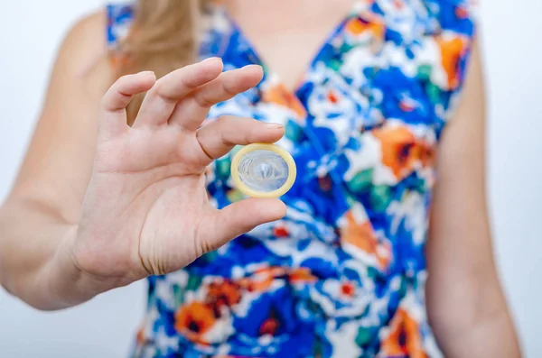 Жінка в кольоровій сукні тримає презерватив в руці без упаковки, демонструє на камеру . — стокове фото
