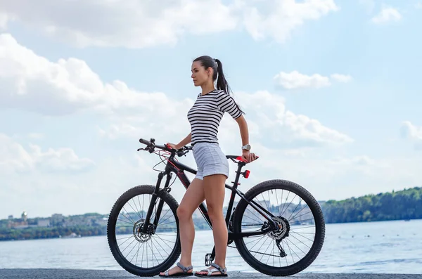 Fitnessmädchen in kurzen weißen Shorts am See mit Fahrrad im Stadtpark — Stockfoto