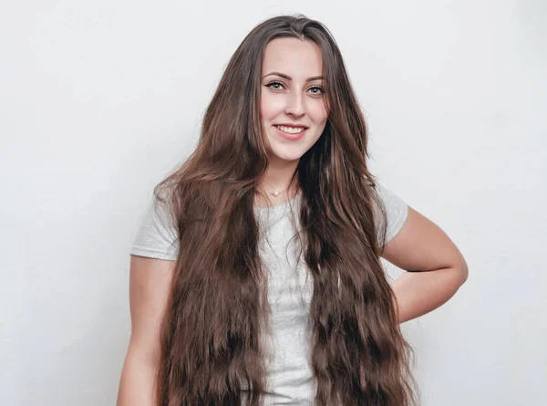 Portrait of a girl with long dark hair on a white background looking at the camera. Pretty smile on face.