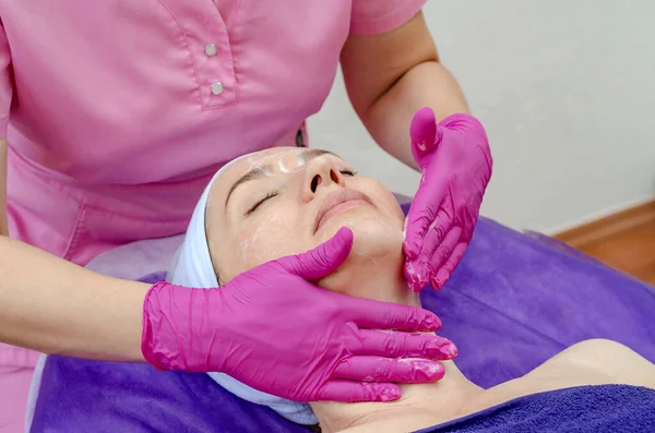 Cosmetologist doctor applies cream to woman face in beauty salon. Preparation for the procedure of rejuvenation, restoration of skin, facial muscles