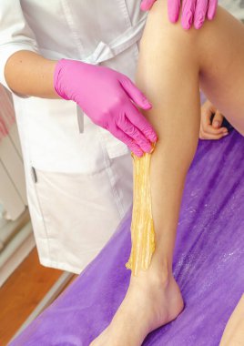 Güzellik uzmanının elleri güzellik salonundaki kızın bacaklarındaki kılları almak için şeker macunu sürüyor..