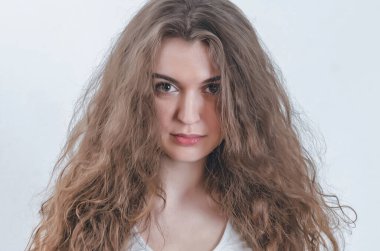 Dalgalı kıvırcık saçlı kız kameraya bakıyor. Alnının altından bak..