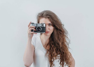 Kıvırcık kız eski bir film kamerasıyla fotoğraf çekiyor. Elinde bir kamera tutuyor..