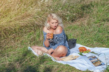 Çimlerin üzerinde battaniyede oturan genç bir kadın. Yaz tatili.