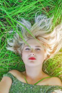 Beyaz saçlı, yeşil çimenlerin üzerinde yatan genç bir kadın. Rahatla, sakin ol, yaz