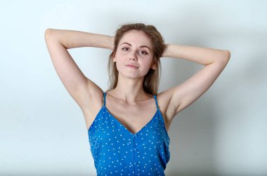 Kahverengi gözlü ve zarif kaşlı güzel beyaz kadın sarı saçlarına dokunuyor. Kollarını başının arkasında tutuyor ve gülümsüyor.