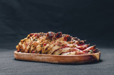 Fragrant slices of baked pork belly on a wooden board, sprinkled with colored peppercorns. Black background. Side view. Meat preparation concept.