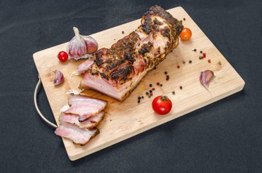 Kesilmiş domuz göbeği. Tahta üzerinde leziz domuz eti dilimleri taze sarımsak karanfilleri, kiraz domatesleri ve renkli biberlerle birlikte. Siyah arka plan. Üst görünüm.