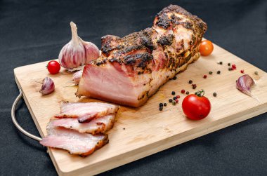 Kesilmiş domuz göbeği. Tahta üzerinde leziz domuz eti dilimleri taze sarımsak karanfilleri, kiraz domatesleri ve renkli biberlerle birlikte. Siyah arkaplan.