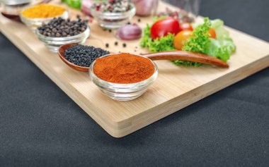 Parlak kırmızı biber ve küçük şeffaf kase. Yakın plan. Tahtadaki baharatlar ve baharatlar arasında kırmızı biber. Siyah masa örtüsü. Aşçılık ilhamı.