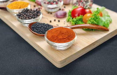 Parlak kırmızı biber ve küçük şeffaf kase. Yakın plan. Tahtadaki baharatlar ve baharatlar arasında kırmızı biber. Siyah masa örtüsü. Aşçılık ilhamı.