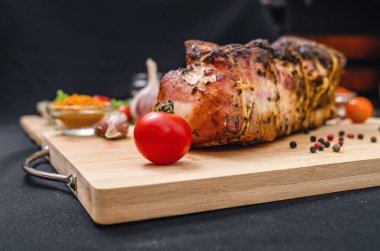 Tahtada taze pişmiş domuz göbeği, soyulmamış sarımsak karanfilleri, kiraz domatesleri ve renkli bezelyeler. Siyah arka plan. Yan görüş. Et pişirme konsepti. Restoran menüsü.