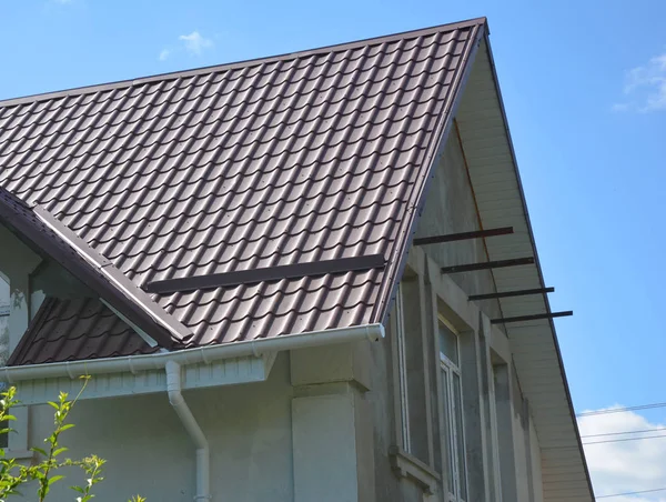 Close up on red metal roof with white, plastic rain gutter system. Roofing Construction.