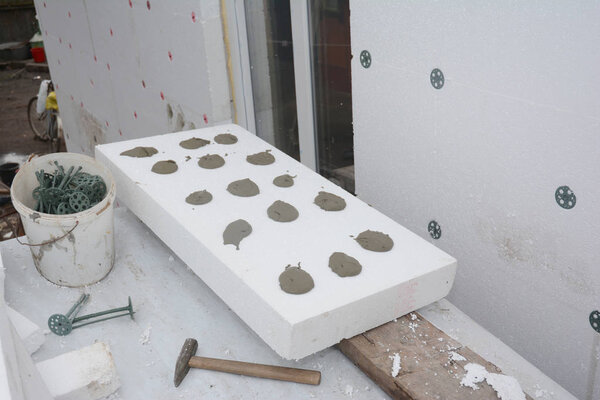 Installing rigid styrofoam insulation board  on house wall for energy saving. Rigid extruded polystyrene insulation with plastic nails, concrete and hammer.