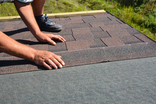 Roofer hands laying Asphalt Shingles on house construction roof. Roofing construction with Asphalt Shingles. 