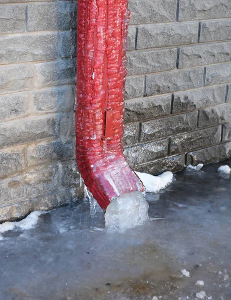 Frozen Gutter, Downspout. Gutter Pipe, Downspouts, House Foundation Wall Sometimes Freeze into Solid Blocks of Ice. Bad rain gutter cleaning.