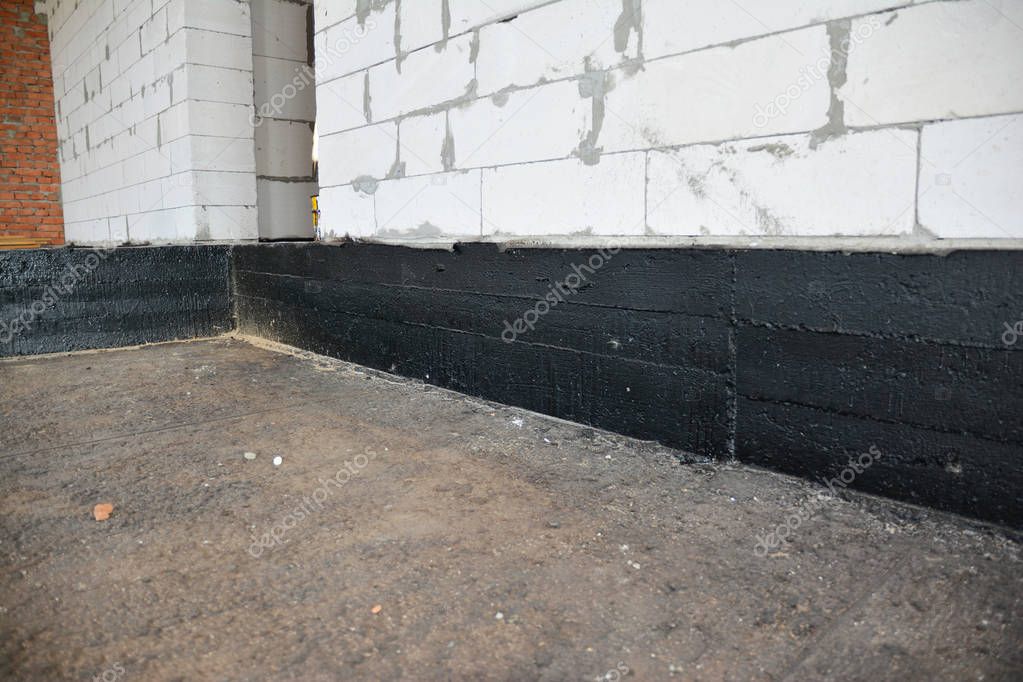 Foundation bitumen waterproofing. Building house construction with waterproofing spray-on tar. Construction techniques for spraying waterproofing basements and foundations.