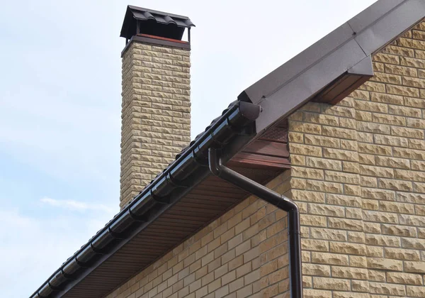 Rain gutter pipe system. Close up on Brick house with roof tiles and plastic roof gutter pipes drain on the corner. Guttering.