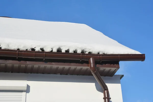 House roof rain gutter in winter, covered ice and snow.