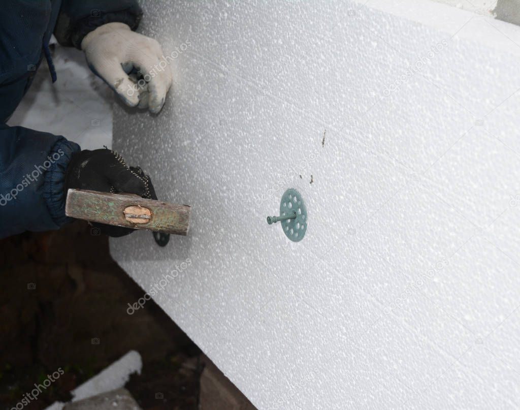 Builder contractor  installing rigid styrofoam insulation board with hammering plastic nail for holding foam insulation.