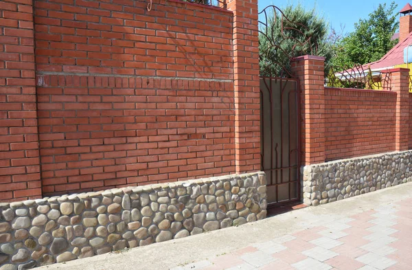 Brick fence with cozy fence sea stone foundation and frame metal door — Stock Photo, Image