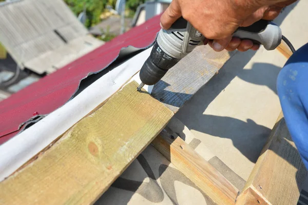 屋根工事写真。ドリルで屋根葺き職人は、金属屋根瓦を敷設する前に、木製の梁、トラス、垂木をインストールします。屋根工事屋根ふき建築業者の金属の屋根シートを敷設. — ストック写真