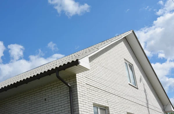 House rooftop with asbestos roof, white bricks and rain gutter