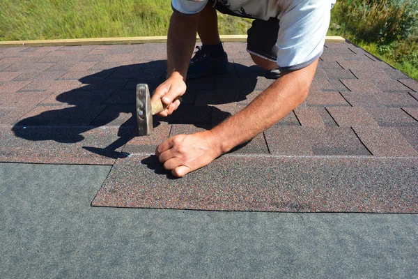 Roofer het installeren van asfalt gordelroos op huis dakbedekking constructie met hamer en nagels in beweging. — Stockfoto