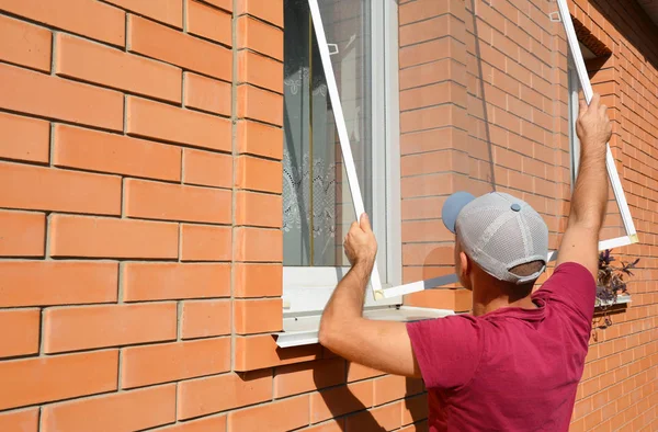 Установка комаров. Рабочий устанавливает экран из комариной проволоки на окно дома для защиты от насекомых . — стоковое фото