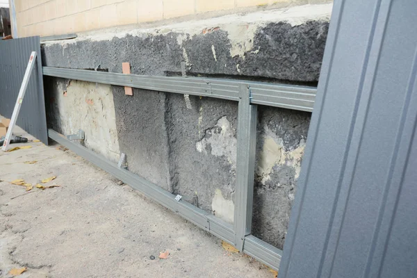Reparação da parede da fundação da casa, renovação com a instalação de folhas de metal na armação de metal para impermeabilização e proteger da umidade da chuva . — Fotografia de Stock