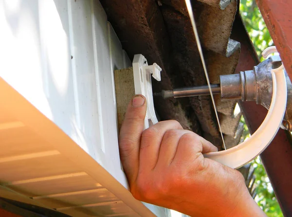 Aannemer installatie plastic dakgoot houder voor downspout afvoerpijp. Plastic dakgoot, regengoot & drainage door klusjesman handen — Stockfoto