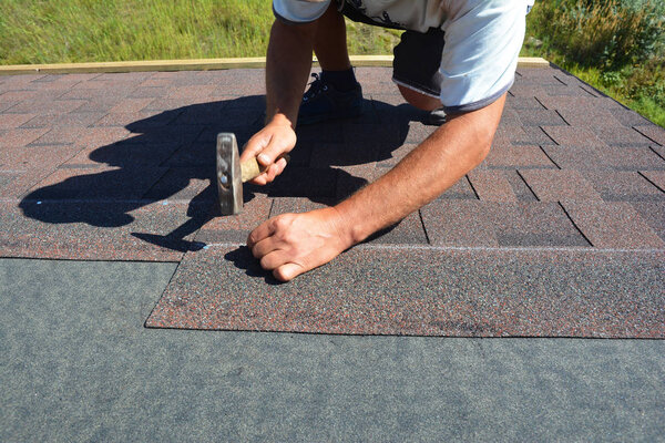 Roofer installing Asphalt Shingles on house Roofing Construction with hammer and nails in motion. 