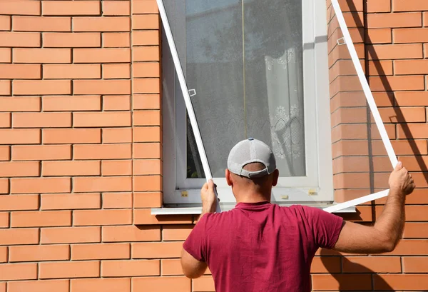 Man installing mosquito net, mosquito wire screen on brick house window — Stock Photo, Image