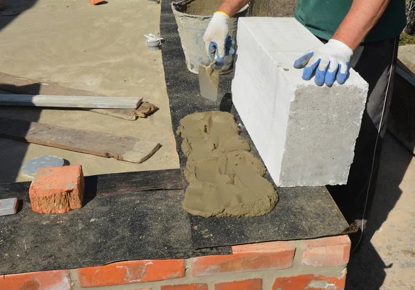 Bricklayer builder laying autoclaved aerated concrete blocks for house foundation wall with waterproofing bitumen membrane — Stock Image Bricklayer builder laying autoclaved aerated concrete blocks for house foundation wall with waterproofing bitumen membrane Stock Photo