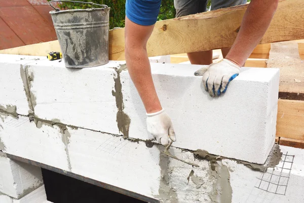 Bricklayer builder laying autoclaved aerated concrete blocks for house wall near unfinished roof wooden beams. — Stock Image Bricklayer builder laying autoclaved aerated concrete blocks for house wall near unfinished roof wooden beams. Royalty Free Stock Images