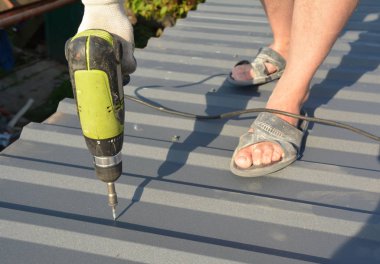 Çatı kiremitleri döşeyen vida tabancalı bir çatı ustası.