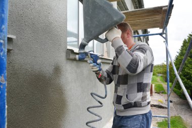 KYIV, UKRAINE - 27 Mayıs 2020: İnşaat inşaatında çalışan bir müteahhit, bina yenileme sırasında sıva havan topu tabancası kullanarak pencerenin etrafındaki dış duvarı sıva, yaprak, sıva ve sıva ile kaplıyor..