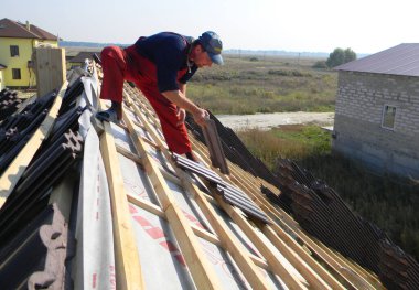 KYIV, UKRAINE - 26 Mayıs 2020: Bir ev inşaatının tepesinde bir bina müteahhidi asfalt kaplı çatı kaplamasına kil seramik fayanslar yerleştiriyor. Çatı inşaatı.