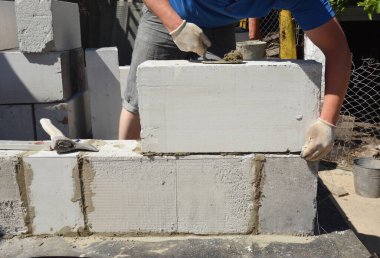 Bir tuğla ustası, büyük gaz, otoklasik beton bloklardan bir duvar örüyor. Bir mala ve balta kullanarak..