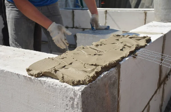 一位建筑承包商正在用大量的砂浆和铲子砂浆 用气体混凝土砌筑新房的墙 — 图库照片