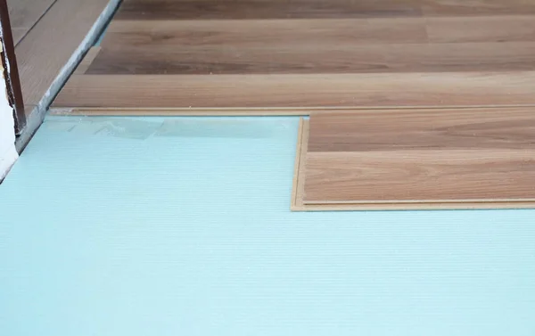 A close-up on wood laminate flooring installation on blue underlayment near the wall.