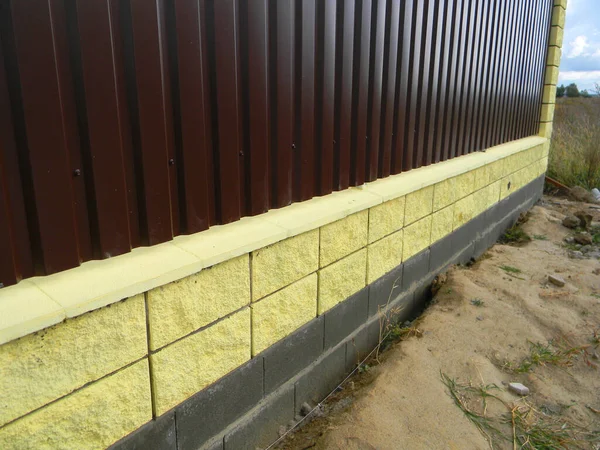 Corrugated metal panel fence installation on the brick foundation in a trench with a level line string set up.