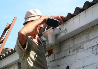 KYIV, UKRAINE - 12 Mayıs 2020: Çatı oluğu kurulumu: Bir inşaat müteahhidi lavabonun üzerinde çalışan bir plastik prizi tamir ediyor ve fasya parantezleri bir elektrikli tornavida kullanarak fasya tahtasına bağlanıyor