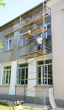 Builder contractor plastering walls with plaster machine before painting walls during facade renovation.