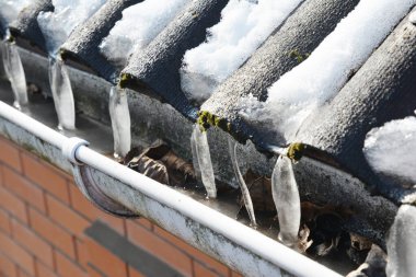 Donmuş plastik yağmur oluğu, kışın buz, buz sarkıtları ve sonbahar yapraklarıyla tıkanmış..