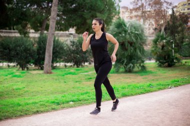 Güzel, genç, sportif bir kadın parkta spor kıyafetlerle koşuyor. Eğitim günü.